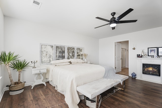 bedroom with a glass covered fireplace, visible vents, baseboards, and wood finished floors