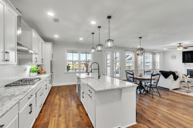 kitchen with dark wood-type flooring, open floor plan, stainless steel gas stovetop, white cabinets, and decorative backsplash