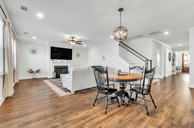 dining room with visible vents, ceiling fan with notable chandelier, stairs, and wood finished floors