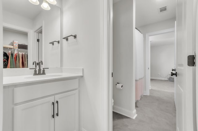 bathroom with visible vents, a walk in closet, toilet, baseboards, and vanity