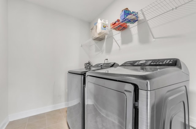 clothes washing area featuring laundry area, light tile patterned floors, baseboards, and washer and clothes dryer