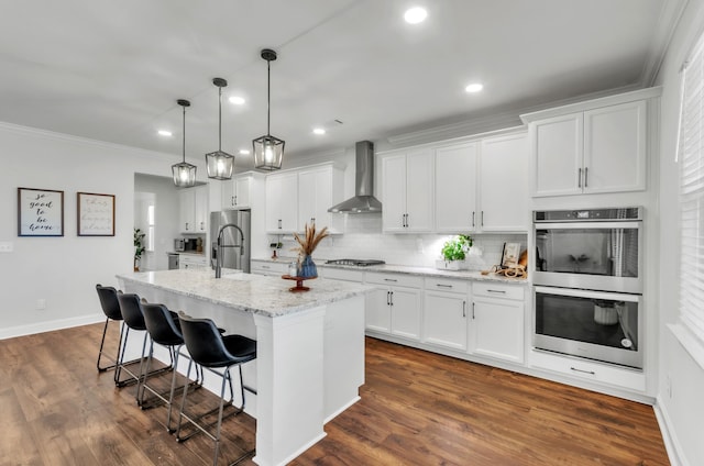 kitchen with wall chimney range hood, a breakfast bar area, decorative backsplash, appliances with stainless steel finishes, and white cabinets