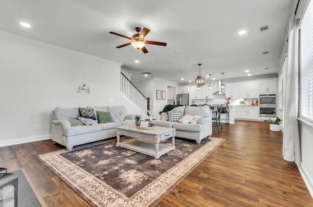 living area featuring stairway, baseboards, recessed lighting, dark wood-type flooring, and ceiling fan with notable chandelier