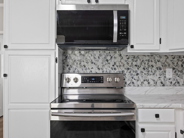 kitchen with tasteful backsplash, white cabinetry, stainless steel appliances, and light stone countertops