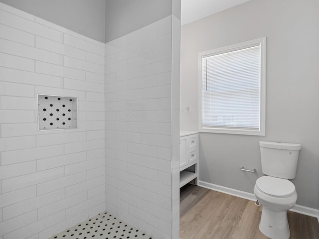 bathroom with vanity, wood finished floors, baseboards, tiled shower, and toilet