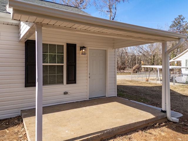 view of exterior entry featuring a patio area, fence, and roof with shingles