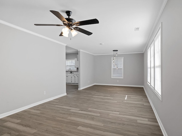 spare room featuring crown molding, baseboards, wood finished floors, a ceiling fan, and a sink