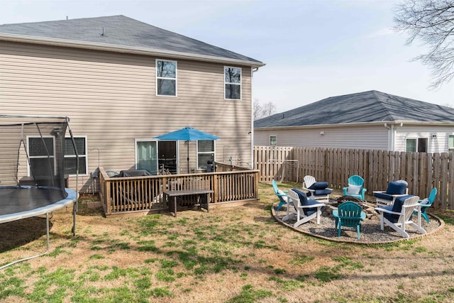 back of property with a trampoline, an outdoor fire pit, a lawn, and fence