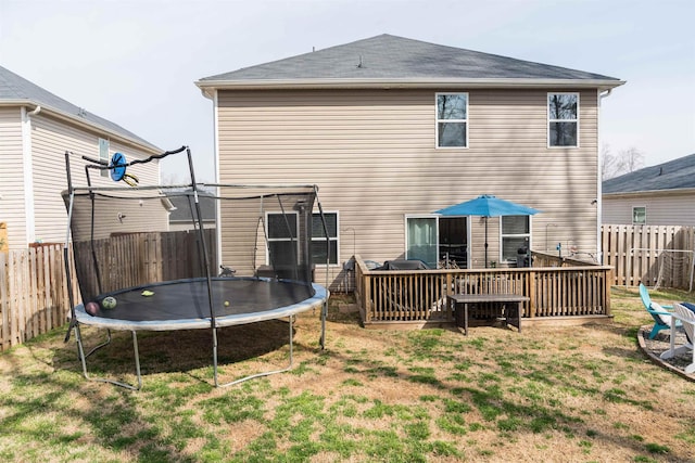 rear view of property with a yard, a trampoline, and a fenced backyard