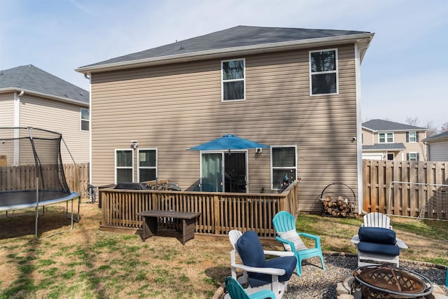 back of property with a yard, a fire pit, a trampoline, and fence