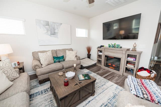 living room with a ceiling fan, a glass covered fireplace, wood finished floors, and visible vents