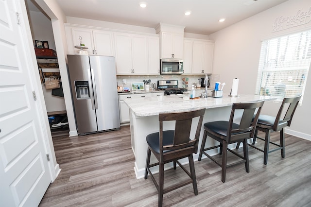 kitchen with tasteful backsplash, light wood finished floors, a center island with sink, a kitchen bar, and stainless steel appliances