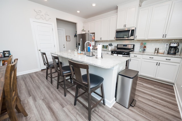 kitchen featuring white cabinets, a center island with sink, backsplash, and stainless steel appliances