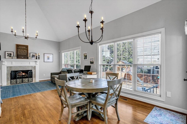 dining space with high vaulted ceiling, wood finished floors, an inviting chandelier, a fireplace, and baseboards