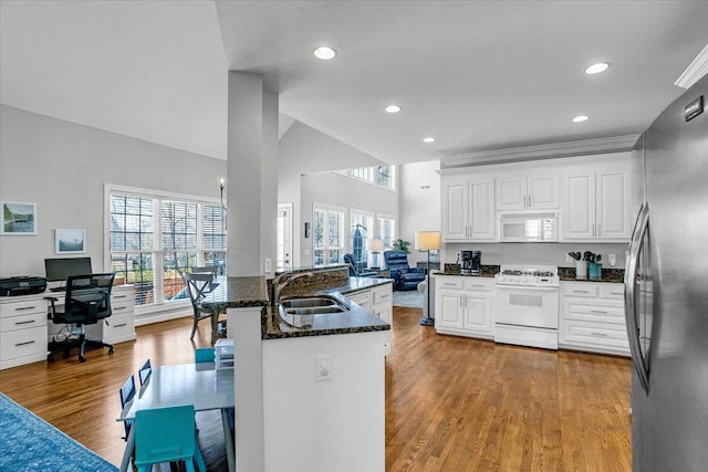 kitchen featuring white appliances, wood finished floors, dark stone counters, a sink, and white cabinets