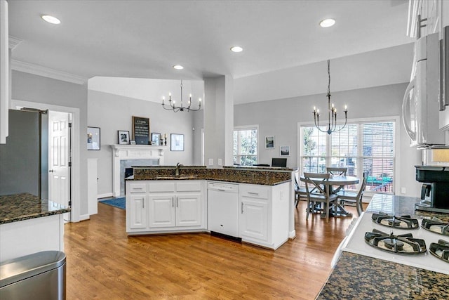 kitchen featuring light wood-type flooring, a notable chandelier, white cabinetry, white appliances, and a fireplace