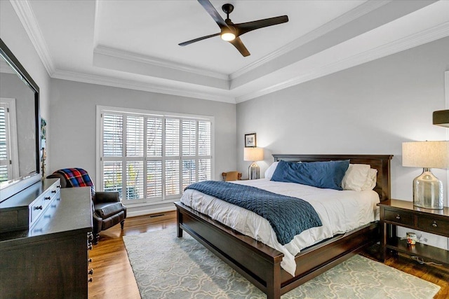 bedroom with wood finished floors, visible vents, ceiling fan, crown molding, and a raised ceiling