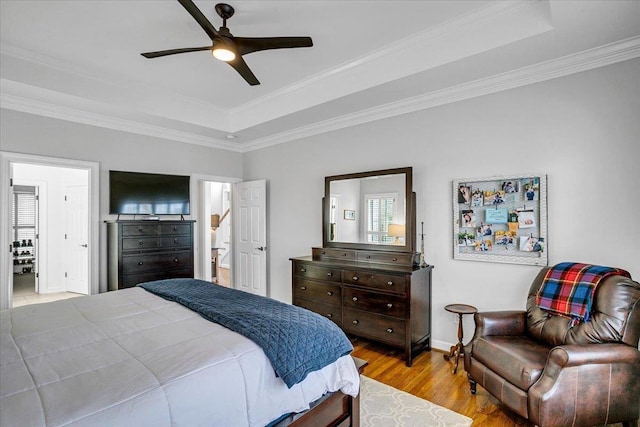 bedroom featuring a ceiling fan, wood finished floors, baseboards, ornamental molding, and a raised ceiling