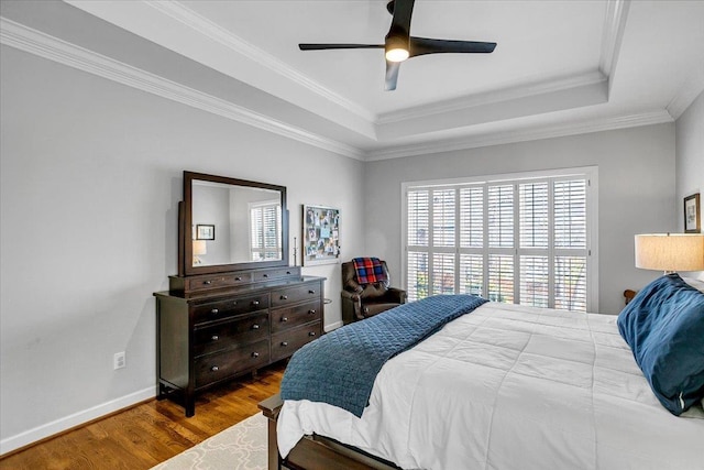 bedroom with a ceiling fan, wood finished floors, baseboards, ornamental molding, and a raised ceiling