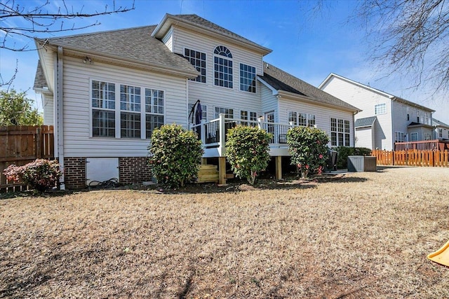 rear view of house featuring a shingled roof, fence, and a wooden deck