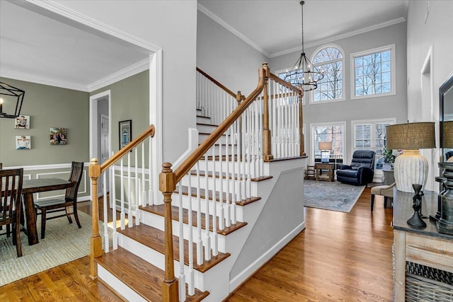 staircase with a notable chandelier, wood finished floors, a towering ceiling, and ornamental molding