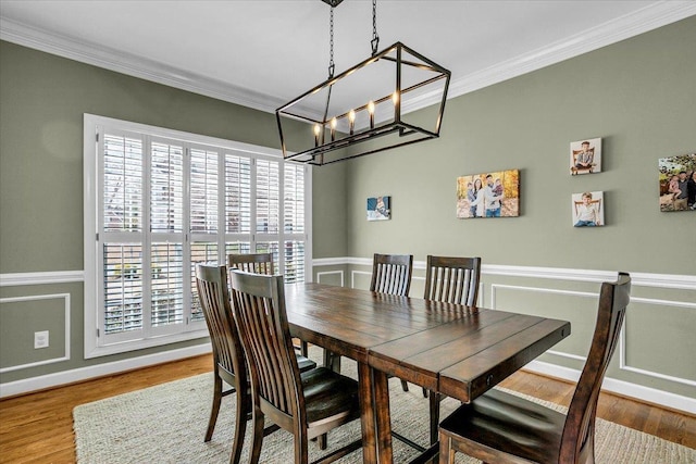 dining area with wood finished floors, a wainscoted wall, ornamental molding, a decorative wall, and a notable chandelier