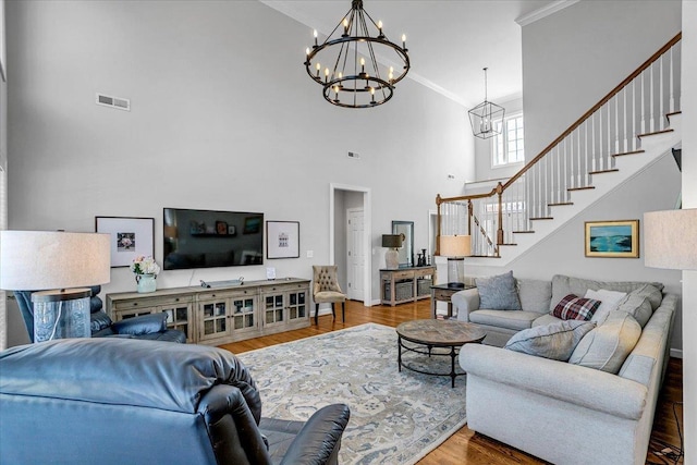 living area featuring wood finished floors, visible vents, ornamental molding, stairs, and a chandelier