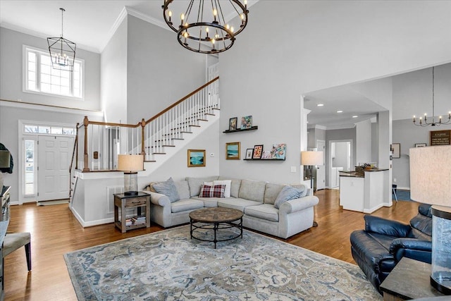 living room with a notable chandelier, wood finished floors, crown molding, a towering ceiling, and stairs