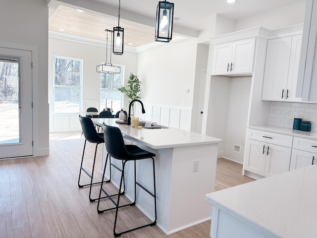 kitchen with light wood-style flooring, a sink, backsplash, white cabinets, and light countertops