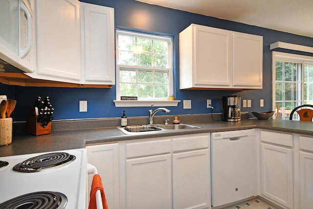 kitchen featuring white appliances, white cabinets, dark countertops, and a sink