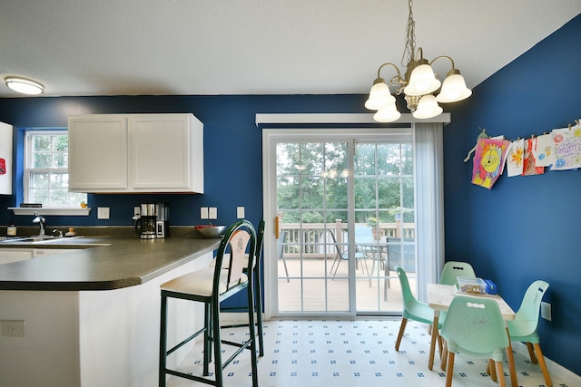 kitchen with dark countertops, a chandelier, a breakfast bar, white cabinets, and a sink