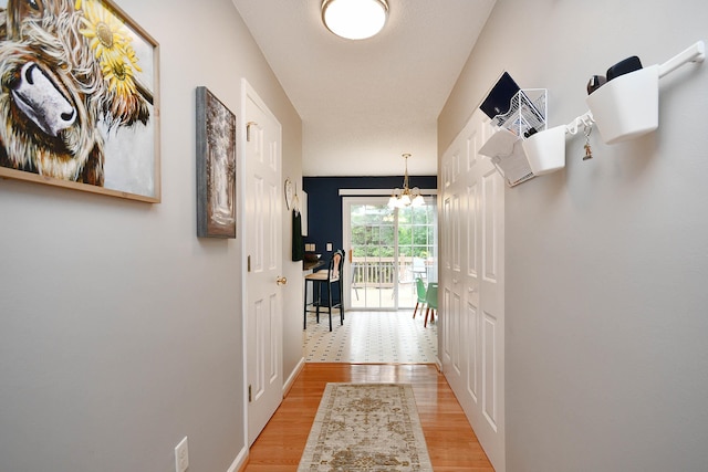 corridor featuring baseboards, light wood finished floors, and a chandelier