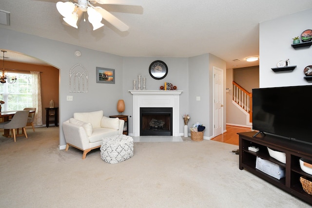 living area with stairway, a fireplace with flush hearth, light carpet, ceiling fan with notable chandelier, and arched walkways