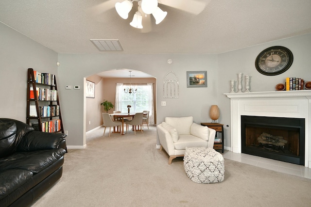 living area with visible vents, ceiling fan with notable chandelier, arched walkways, a fireplace, and light colored carpet