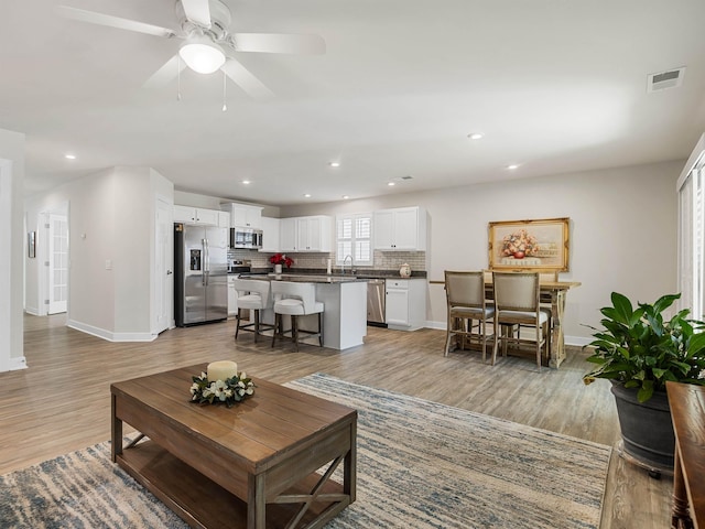 living area featuring visible vents, baseboards, a ceiling fan, and light wood finished floors