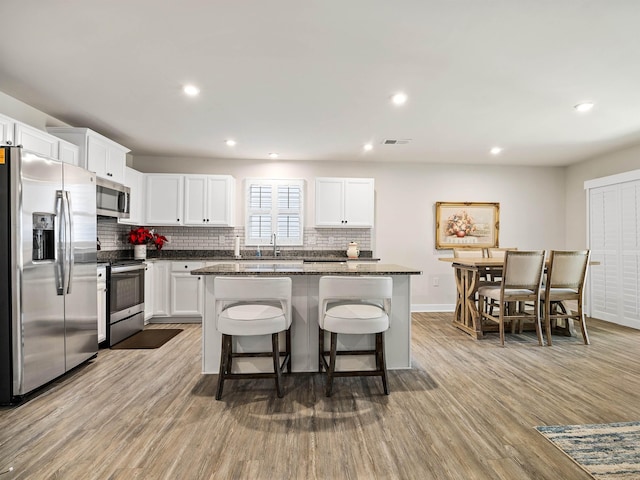 kitchen featuring wood finished floors, visible vents, decorative backsplash, appliances with stainless steel finishes, and a center island