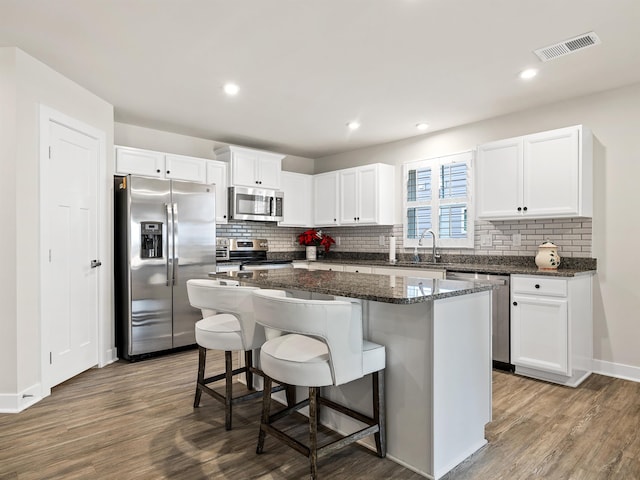 kitchen with visible vents, dark wood-type flooring, a center island, stainless steel appliances, and white cabinets