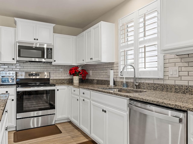 kitchen featuring a sink, tasteful backsplash, white cabinetry, stainless steel appliances, and light wood-style floors