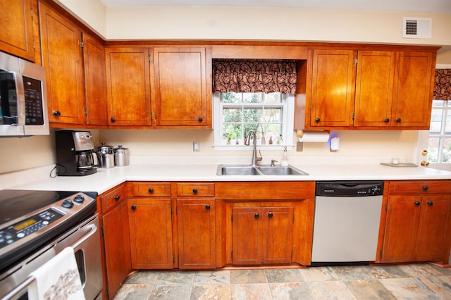 kitchen with visible vents, light countertops, appliances with stainless steel finishes, brown cabinetry, and a sink