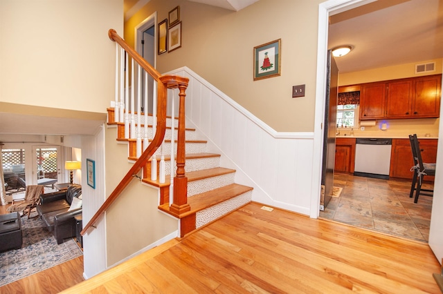 staircase with a wainscoted wall, wood finished floors, and visible vents