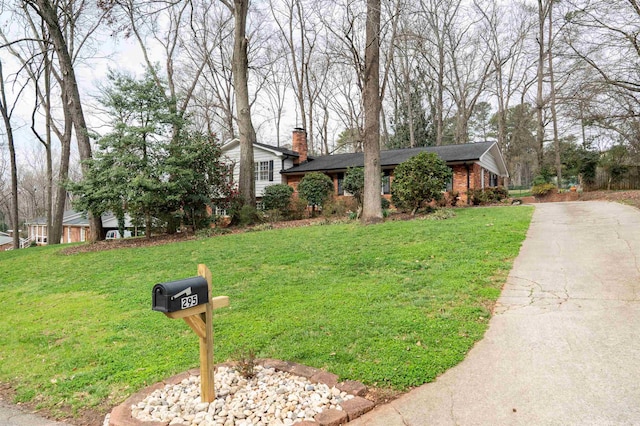 view of front facade featuring a front yard, concrete driveway, brick siding, and a chimney