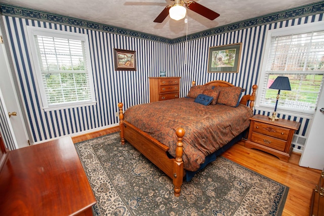 bedroom with baseboards, a textured ceiling, wood finished floors, and wallpapered walls