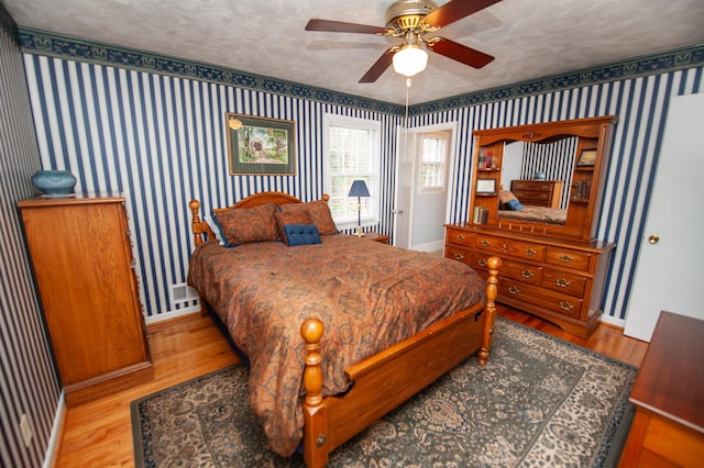 bedroom featuring baseboards, a textured ceiling, wood finished floors, and wallpapered walls