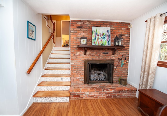 stairs featuring a brick fireplace, wood finished floors, and crown molding