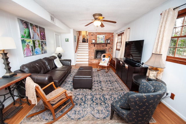 living room with visible vents, a brick fireplace, baseboards, wood finished floors, and a ceiling fan