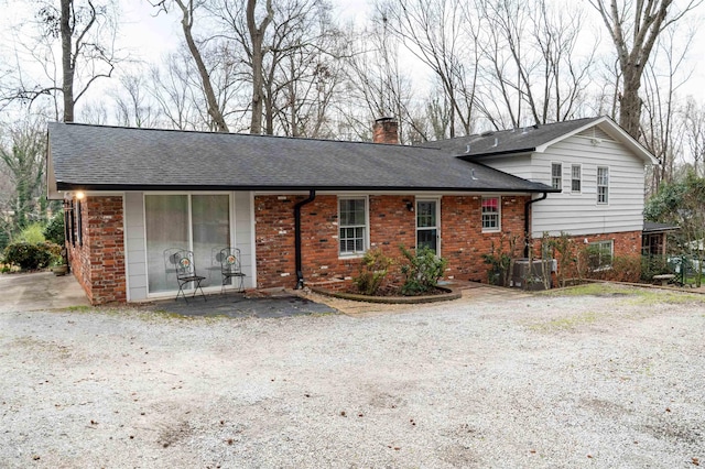 view of front of property featuring a shingled roof, brick siding, and a chimney