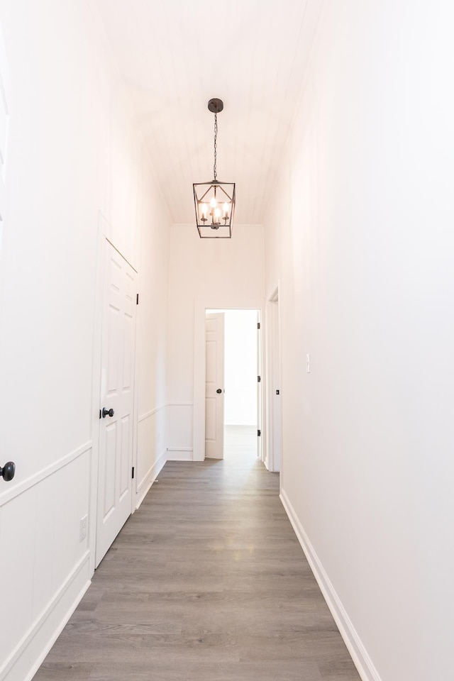 corridor with light wood-style flooring, baseboards, and a chandelier