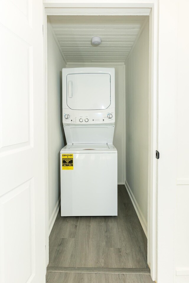 laundry area with laundry area, stacked washer and dryer, wood finished floors, and baseboards