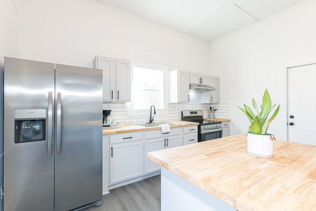 kitchen featuring backsplash, wooden counters, under cabinet range hood, stainless steel appliances, and a sink