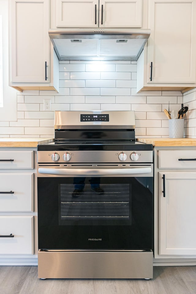 kitchen featuring stainless steel electric range, exhaust hood, white cabinets, light wood finished floors, and decorative backsplash